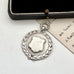 Vintage silver watch fob on a white surface with a black box and paper in the background.