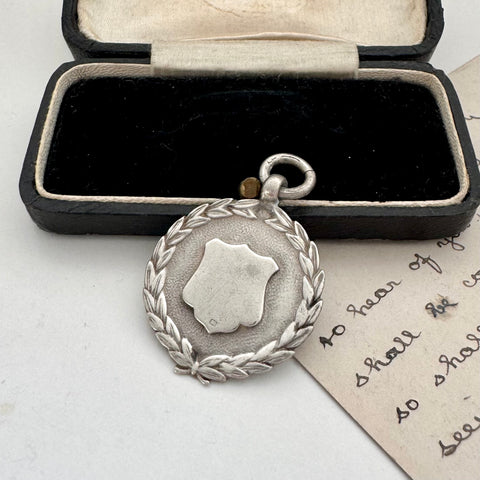 Silver medal with wreath design in an open box on a white surface
