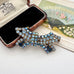 A vintage-style rhinestone brooch in a bow shape, featuring light blue, dark blue, and iridescent blue stones set in gold-toned metal, displayed next to its open vintage presentation box on a light surface.