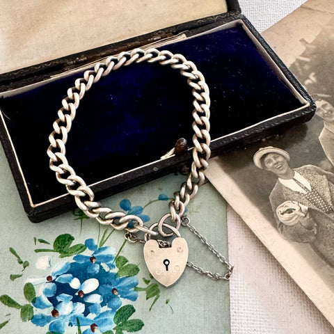 Silver chain bracelet with a heart-shaped lock charm on a floral and vintage-style background