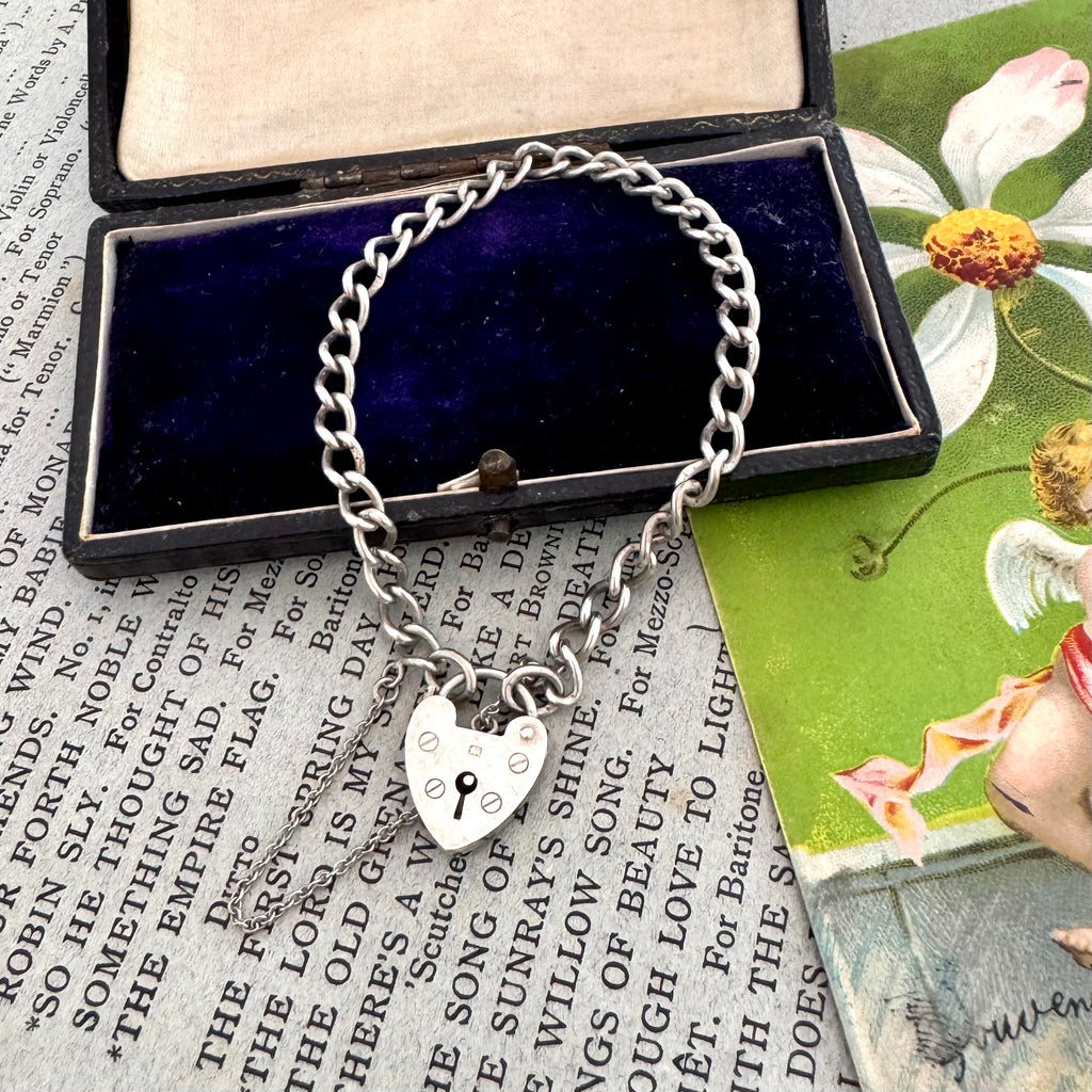 Vintage silver bracelet with heart-shaped lock charm in an open jewelry box on vintage paper.