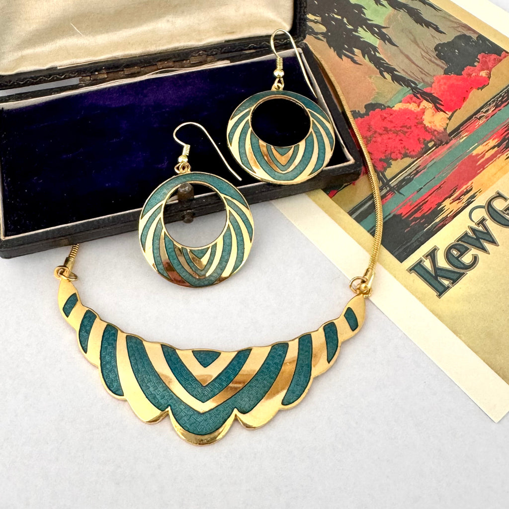 A gold and teal enamel jewelry set featuring a scalloped statement necklace and matching circular drop earrings, displayed with a velvet jewelry box and a vintage-style card.