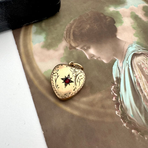 Vintage heart-shaped locket with a red stone on an old photograph of a woman.