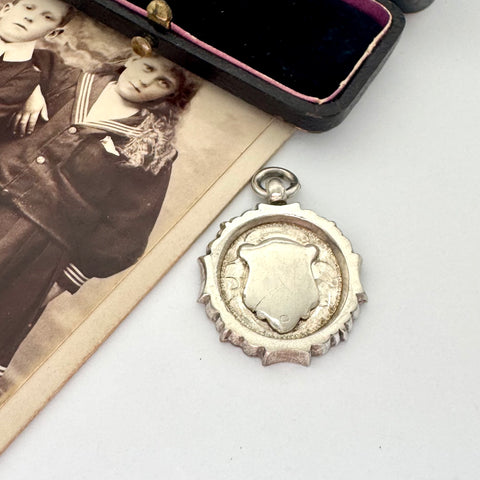 Vintage 1937 Chester silver watch fob on a white surface next to an open box with velvet interior.