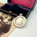 Vintage 1937 Chester silver watch fob on a white surface next to an open box with velvet interior.