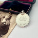 Vintage silver medal with engraved text next to an old photograph on a white surface
