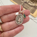 Necklace with a vintage Infant of Prague charm held by a hand, with a vintage-style card in the background.