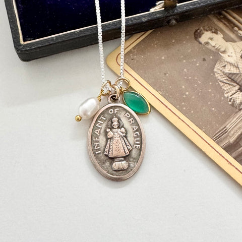 Necklace with a pendant labeled 'Infant of Prague' on a white surface with an old photograph in the background.