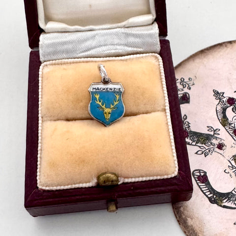 Jewelry box with a vintage silver charm featuring a coat of arms and 'MACKENZIE' text on a white background.