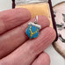 Jewelry box with a vintage silver charm featuring a coat of arms and 'MACKENZIE' text in a womans hands.