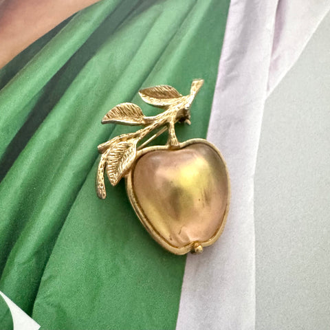 Rare GB stamped Sarah Coventry gold apple-shaped brooch with leaves on a green and white fabric background