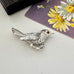 Vintage Sarah Coventry silver bird-shaped brooch with a red gemstone with a vintage postcard