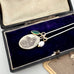 Vintage religious pendant with chain and green leaf charm in an open jewelry box