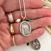 Hand holding a silver necklace with a Saint Paul pendant and green leaf charm.