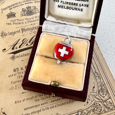 Vintage Swiss silver and red enamel cowbell charm in an open jewelry box on a vintage newspaper background