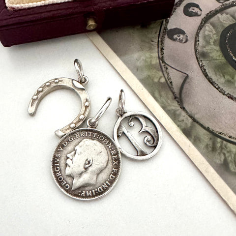 A vintage silver horseshoe charm, no 13 charm and a 1918 British threepence on a white background with an old postcard in the corner.