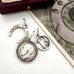 A vintage silver horseshoe charm, no 13 charm and a 1918 British threepence on a white background with an old postcard in the corner.