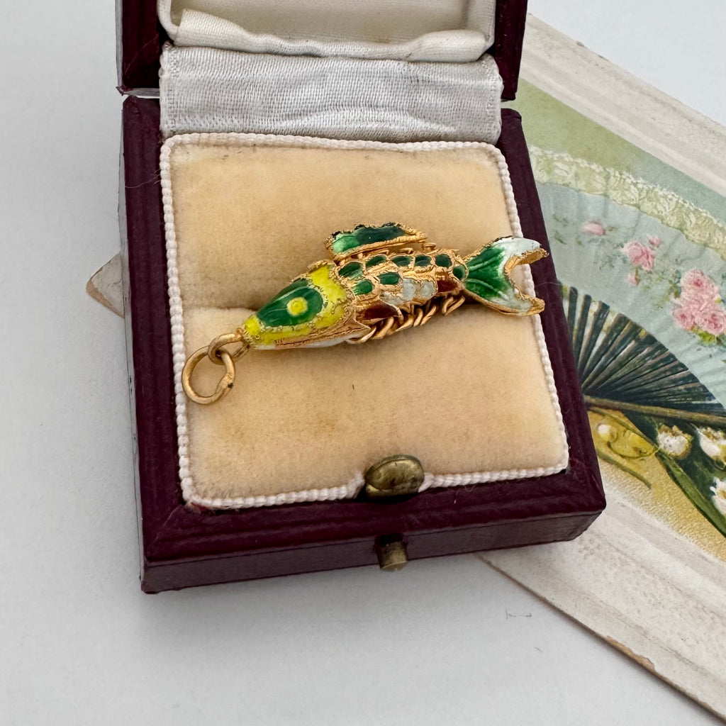 Vintage articulated fish charm in a box with a vintage postcard in the background