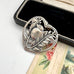 Silver bird and leaf design on a heart-shaped pendant with a black box in the background.