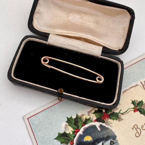 Gold collar safety pin in an open black jewelry box with a decorative card in the background