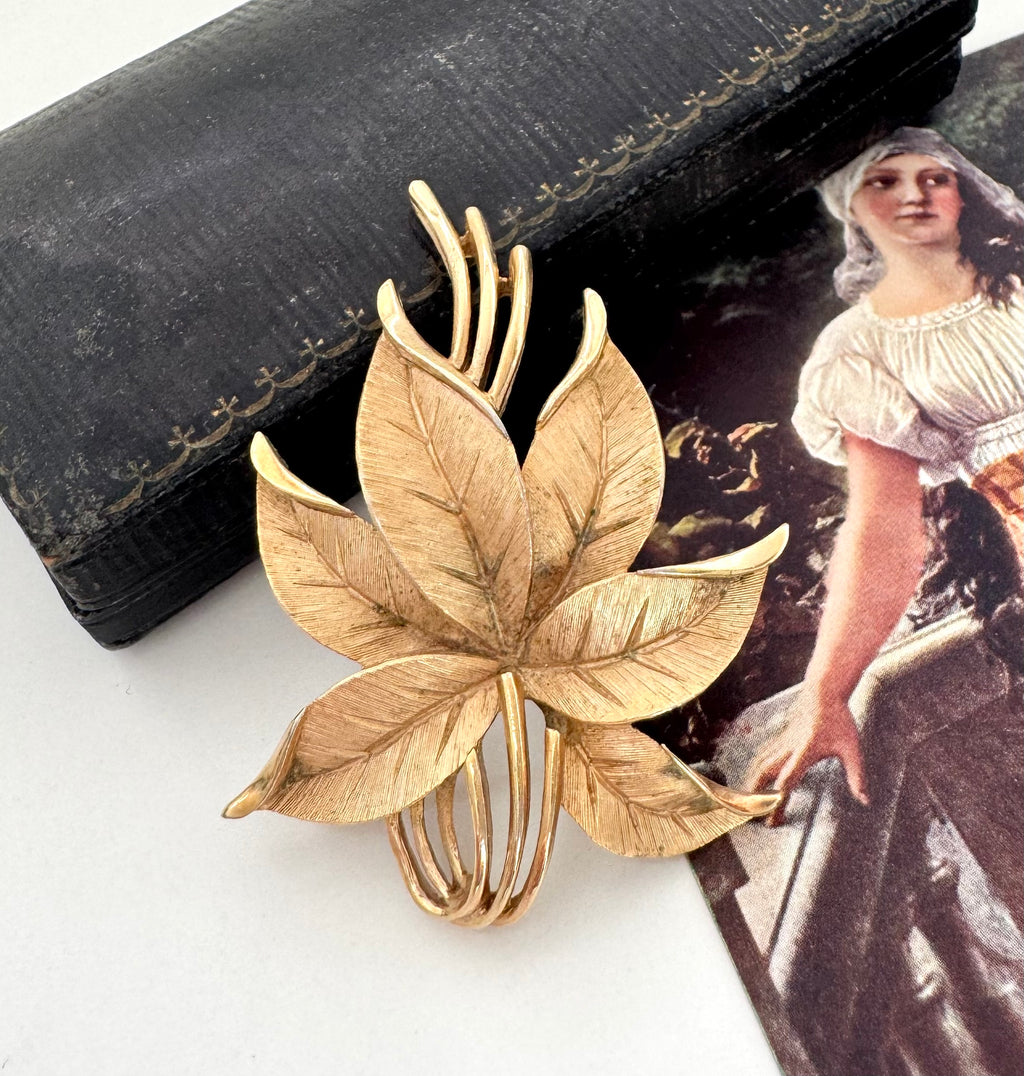 Vintage Crown Trifari leaf-shaped brooch on a white surface with a vintage-style magazine in the background.