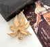 Vintage Crown Trifari leaf-shaped brooch on a white surface with a vintage-style magazine in the background.