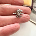 Silver Dusty Bin charm held between fingers on a neutral background