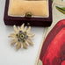 Floral brooch on a white surface with a vintage-style card and box in the background