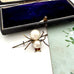 Spider-shaped brooch with pearls on a white surface next to an open jewelry box.