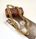 A chunky French vintage rolled gold chain necklace draped over a vintage brown textured box and a black-and-white print featuring the name 'ASTA NIELSEN'.
