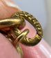 Close-up of a gold-toned metal ring or clasp with the word 'GARANTIE' engraved on a circular loop, held between fingers.