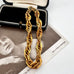 A chunky gold chain bracelet with a thick, twisted rope-like link design, displayed inside an open black jewelry box on top of a vintage black-and-white photograph.
