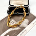 A chunky gold chain link bracelet displayed on top of an open black jewelry box, with a vintage black-and-white photograph underneath.