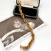 A thick gold chain bracelet with a lobster clasp, draped over an open black jewelry box and a vintage black-and-white photograph card featuring the name Asta Wilson.