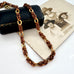 A vintage-Jakob Bengel Byzantine chain necklace with interwoven copper and gold links, draped over a black leather case and an old sepia-toned family photograph on a white surface.