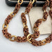 A close up of a vintage-Jakob Bengel Byzantine chain necklace with interwoven copper and gold links, draped over a black leather case and an old sepia-toned family photograph on a white surface.