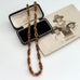 A vintage-Jakob Bengel Byzantine chain necklace with interwoven copper and gold links, draped over a black leather case and an old sepia-toned family photograph on a white surface.