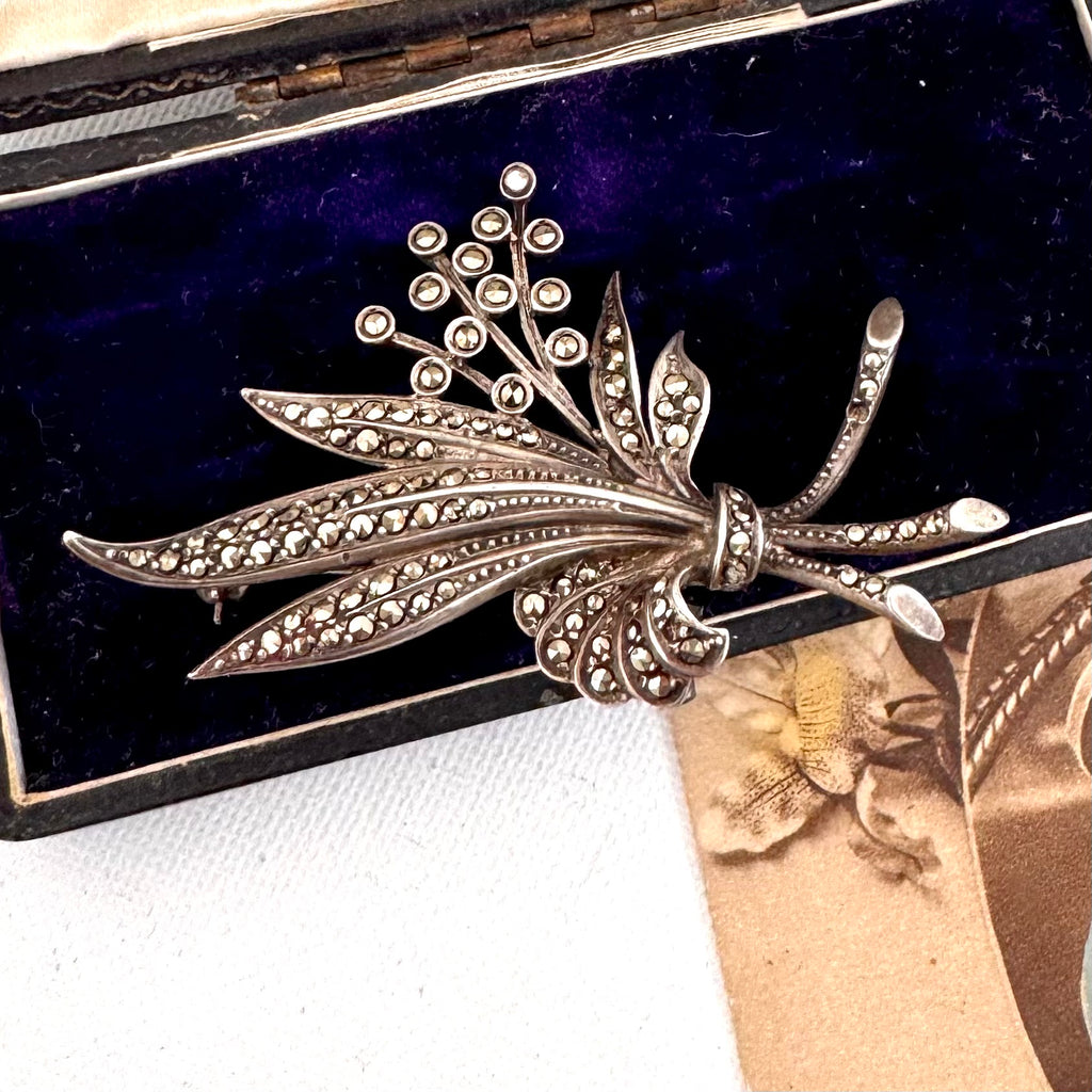 Vintage marcasite and silver brooch with floral design on a dark blue background