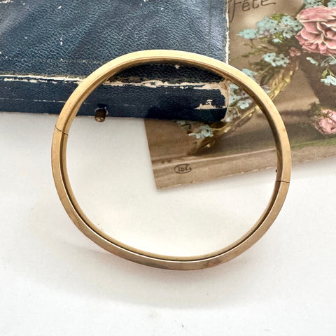 Gold bracelet on a white surface with a floral card in the background