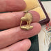 Gold kiwi bird pendant held between fingers with a textured background