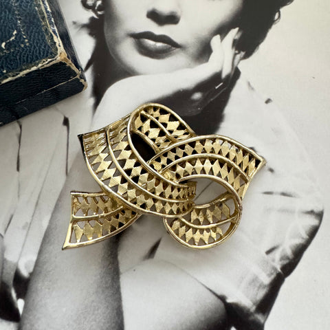 Vintage gold tone bow brooch with geometric design on a black and white background