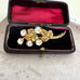 Gold vintage brooch with clear stones and ivy leaf details in an open jewelry box on a textured surface