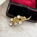 Gold brooch with leaf design and clear stones on a textured surface
