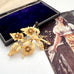 Vintage gold tone floral brooch with a vintage-style box and image in the background
