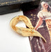 Gold brooch on a white surface with a vintage-style magazine in the background
