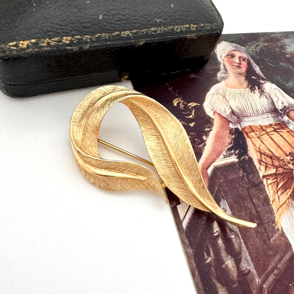 Gold feather-shaped Sarah Coventry brooch on a vintage-style card with a woman