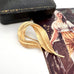 Gold feather-shaped Sarah Coventry brooch on a vintage-style card with a woman