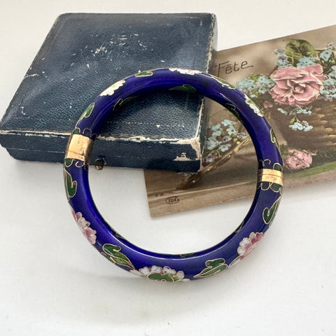 Blue vintage cloisonne floral bracelet on a white surface with an old book and card in the background