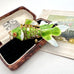 An vintage koi fish-shaped pendant with green and white enamel scales and gold wire detailing, displayed inside an open vintage brown presentation box with a black velvet lining.
