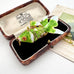 A vintage Koi fish pendant with green enamel scales and gold-toned metal details, displayed inside an open antique presentation box with a black velvet lining.